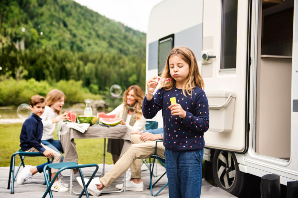 Barnfamilj utanför husbil under campingsemester på campingplats.