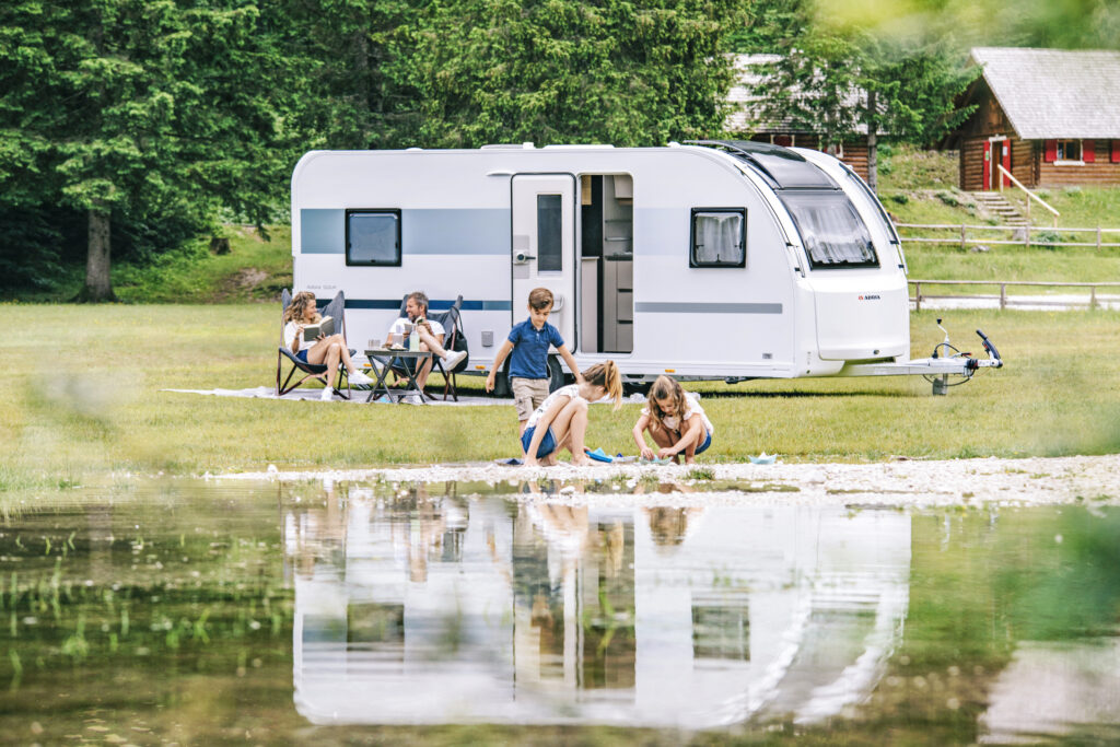 Husvagn vid sjö under sommarcamping med familj.